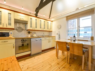 A kitchen with cream cabinets a wooden dining table with chairs and kitchen appliances at Chough Cottage in Kingsand And Cawsand