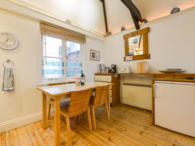 A kitchen dining area with wooden table and chairs a window a wall clock and kitchen appliances at Chough Cottage in Kingsand And Cawsand