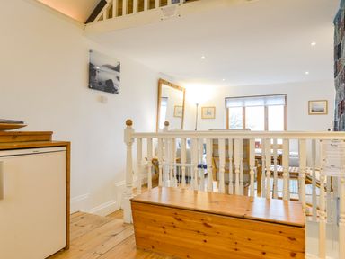 An interior room with wooden floors white railings a wooden chest and a seating area with a large window at Chough Cottage Kingsand And Cawsand