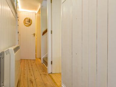 A narrow hallway with wooden floor and white paneled walls at Chough Cottage in Kingsand And Cawsand