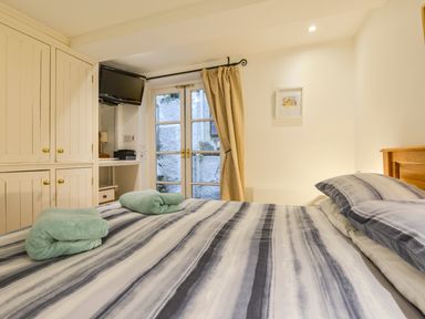 A bedroom with a bed, striped bedding, towels on the bed, wardrobe, wall-mounted TV, window with curtains at Chough Cottage in Kingsand And Cawsand