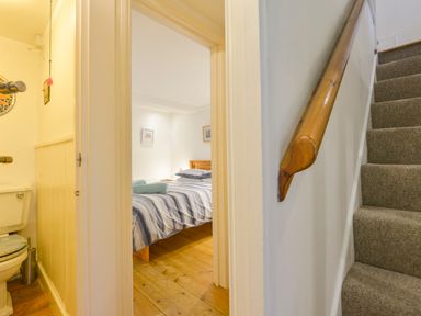 Carpeted staircase with wooden handrail next to doorway showing bathroom and bedroom with striped bedding at Chough Cottage in Kingsand And Cawsand
