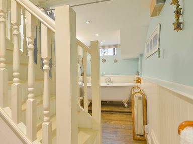 A bathroom with a clawfoot bathtub wooden floor and white banisters at Chough Cottage in Kingsand And Cawsand