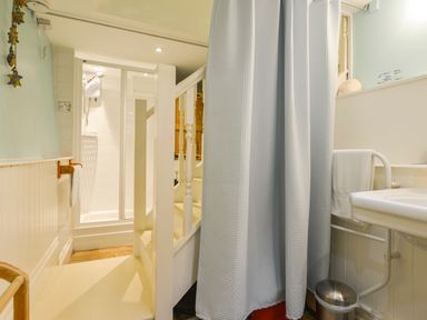 A bathroom with a shower, a sink, a towel rack, and stairs with a white railing at Chough Cottage in Kingsand And Cawsand