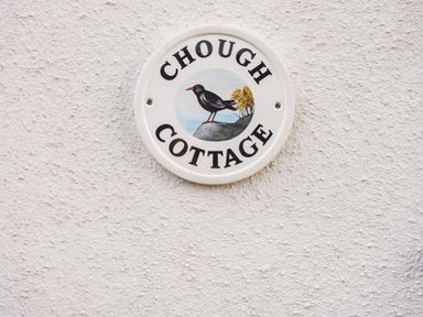 A round sign on a textured wall with a bird and the text Chough Cottage