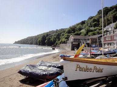 A beach with boats and a building near a forested hill at Chough Cottage in Kingsand And Cawsand