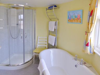 A bathroom with a shower enclosure bathtub chair towel rack and window with patterned curtains at Balcony Cottage in Kingsand And Cawsand
