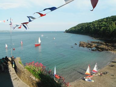 A coastal view with sailboats on the water and a rocky shore with boats and people near the beach at Balcony Cottage in Kingsand And Cawsand
