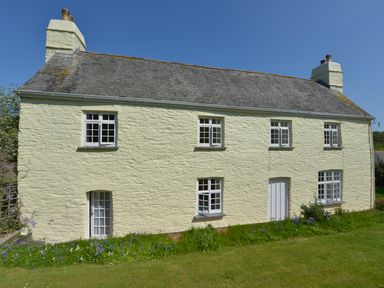A two-story stone house with multiple windows and a door in a grassy garden at Tregonhawke Farmhouse in Millbrook
