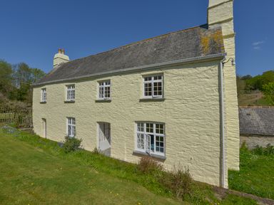 Exterior view of a two story cream colored farmhouse with multiple windows and a sloped roof at Tregonhawke Farmhouse Millbrook