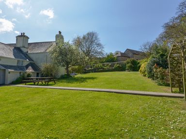 A garden with picnic tables and trees next to a house at Tregonhawke Farmhouse in Millbrook