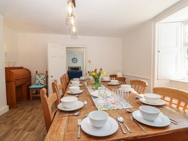 A dining room with a long wooden table set for a meal at Tregonhawke Farmhouse in Millbrook