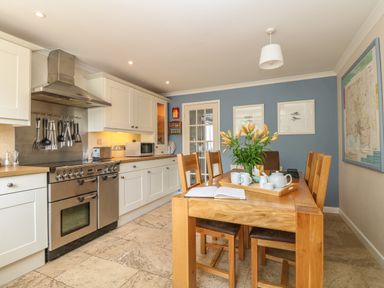 A kitchen with white cabinets a stainless steel stove and a wooden dining table with chairs and flowers at 1 River Cottage in Calstock
