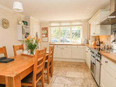 A kitchen with a wooden dining table and chairs white cabinets and a window overlooking trees at 1 River Cottage in Calstock