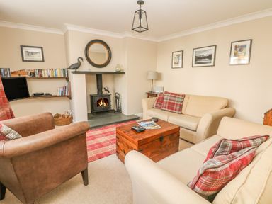 A living room with two beige sofas a brown armchair a wooden chest coffee table a fireplace and wall shelves with books at 1 River Cottage Calstock