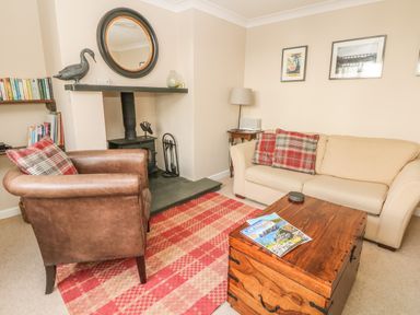 A living room with a beige sofa and brown armchair near a fireplace with a round mirror and a wooden chest coffee table at 1 River Cottage in Calstock