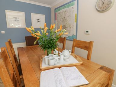 A dining table with a flower vase mugs teapot and an open notebook on it in a room with blue and cream walls at 1 River Cottage in Calstock