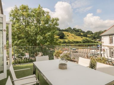 An outdoor patio with white table and chairs overlooking a tree hill and river at 1 River Cottage in Calstock