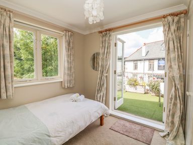 A bedroom with a single bed near windows and open double doors leading to a balcony at 1 River Cottage in Calstock