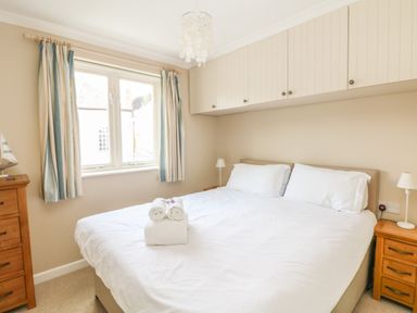 A bedroom with a double bed white bedding bedside tables with lamps window with striped curtains and wall cabinets at 1 River Cottage in Calstock