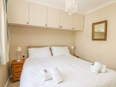 A bedroom with a double bed white linens wooden bedside tables and wall cabinets at 1 River Cottage in Calstock