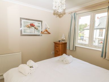 A bedroom with a bed with white linens and rolled towels a wooden chest of drawers and a window with striped curtains at 1 River Cottage in Calstock
