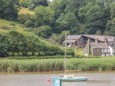 A boat on a river with houses and trees in the background at 1 River Cottage in Calstock