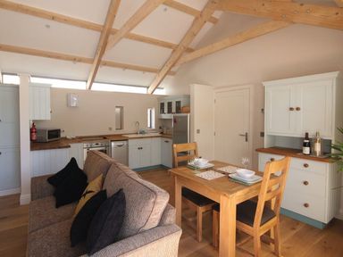 A kitchen and dining area with wooden beams on the ceiling a wooden dining table and chairs a sofa and white cabinets at Mugwell Barn Luckett near Callington