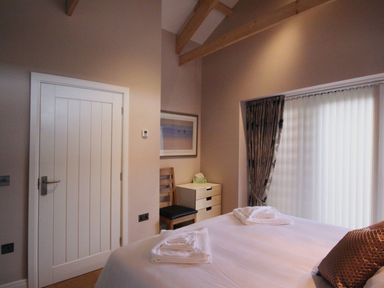 A bedroom with a bed towels a wooden chair a small chest of drawers and a window with curtains at Mugwell Barn Luckett near Callington