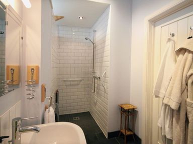 A bathroom with a walk-in shower with tiled walls a sink mirror and towels at Mugwell Barn Luckett near Callington