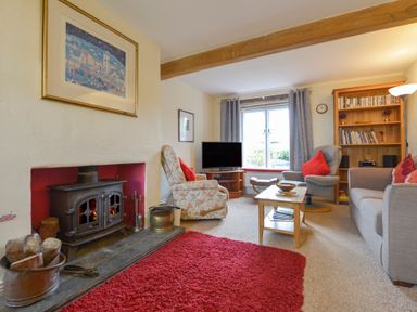 A living room with a wood-burning stove red rug armchairs sofa coffee table and bookshelf at Regatta Cottage in Feock