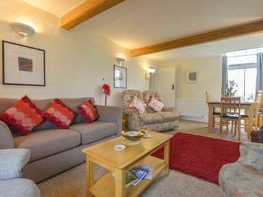 A living room with sofa and armchairs a coffee table with magazines a dining table near a window at Regatta Cottage in Feock