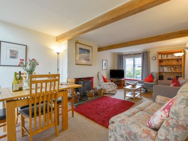 A living room and dining area with wooden beams a fireplace a red rug and seating at Regatta Cottage in Feock