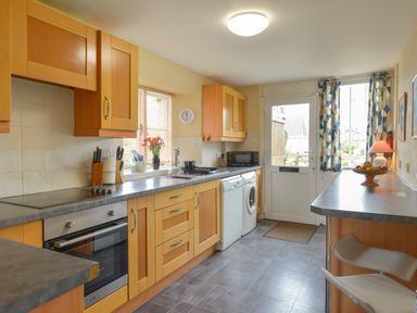 A kitchen with wooden cabinets countertop appliances and a table with chairs at Regatta Cottage in Feock
