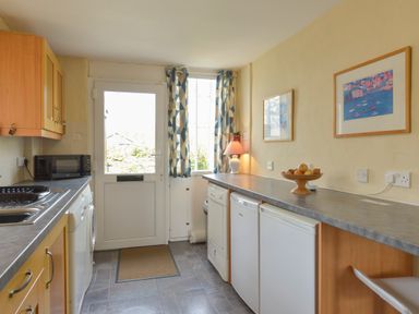 A kitchen with a countertop microwave sink dishwasher refrigerators and a door with a window at Regatta Cottage in Feock