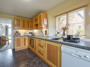 A kitchen with wooden cabinets a dishwasher a sink and a window with blinds at Regatta Cottage Feock