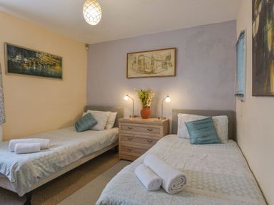 A bedroom with two single beds towels on beds a chest of drawers with lamps and flowers at Regatta Cottage in Feock