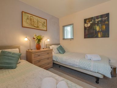 A bedroom with two single beds a wooden chest of drawers with lamps and a vase of flowers on top and two paintings on the walls at Regatta Cottage in Feock