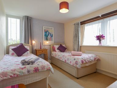 A bedroom with two single beds with floral bedding and purple pillows at Regatta Cottage in Feock