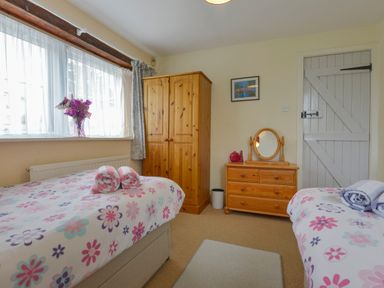 A bedroom with two beds with floral bedspreads a wooden wardrobe wooden dresser with mirror and a window with curtains at Regatta Cottage in Feock
