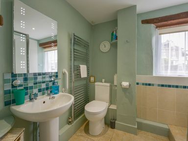A bathroom with a sink mirror towel rack toilet and window at Regatta Cottage in Feock