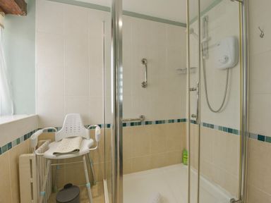 A shower room with a shower chair a grab bar and a shower unit at Regatta Cottage in Feock