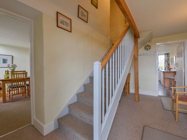 A staircase with framed pictures on the wall and doorways leading to a dining room and kitchen at Regatta Cottage in Feock