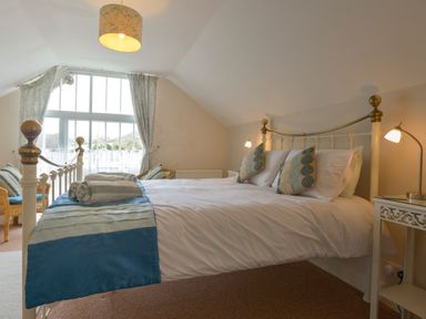 A bedroom with a bed with pillows and folded towels next to a large window at Regatta Cottage in Feock