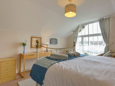 A bedroom with a bed and rolled towels on it a desk a mirror and a window with curtains at Regatta Cottage in Feock