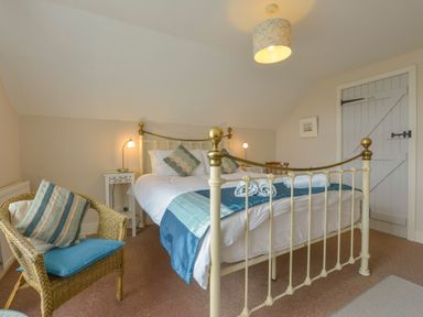 A bedroom with a metal bed frame blue and white bedding and a wicker chair at Regatta Cottage Feock