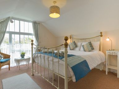 A bedroom with a metal bed frame a small table with a plant and a wicker chair at Regatta Cottage in Feock