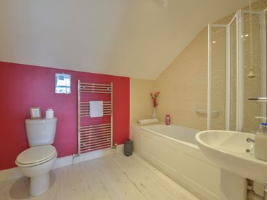 A bathroom with a toilet, towel rail, bathtub, shower screen, washbasin, and decorative flowers at Regatta Cottage in Feock