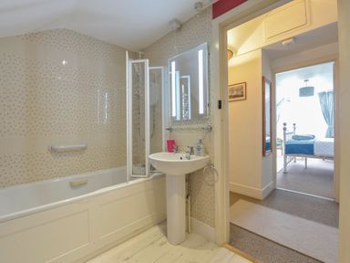 A bathroom with a bathtub shower screen pedestal sink and a mirror leading to a bedroom at Regatta Cottage in Feock