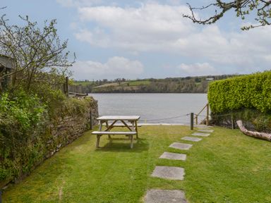 A garden with a picnic table and stone path leading to a body of water at Regatta Cottage in Feock